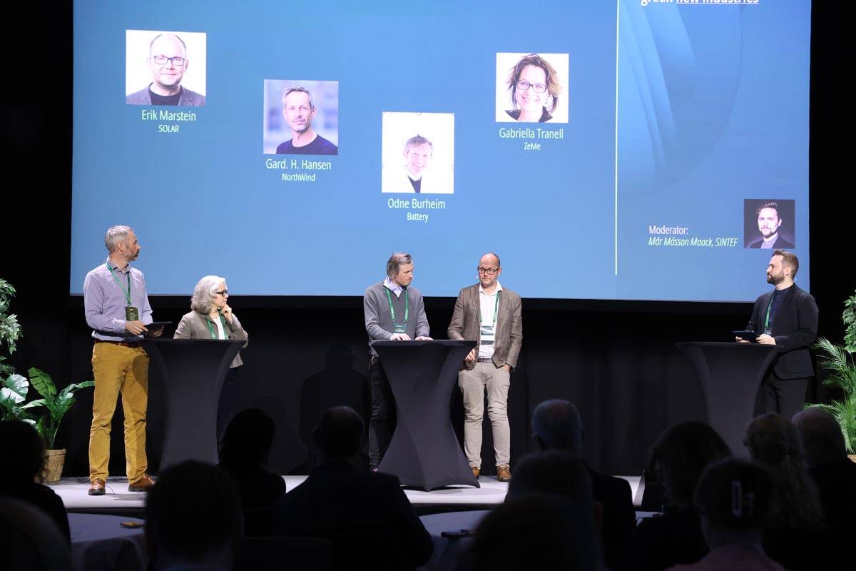 A group of people discussing on a stage, at a conference.